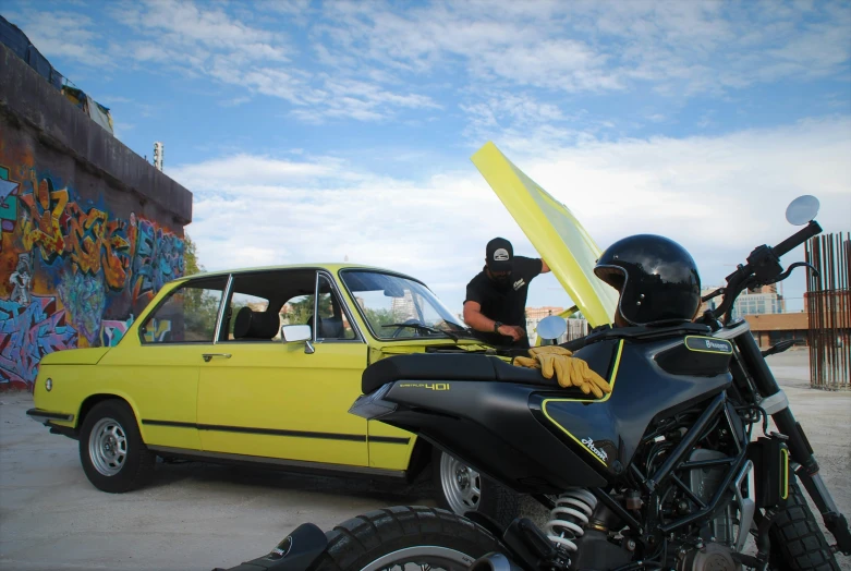 a person in black shirt standing next to a yellow car and motorcycle