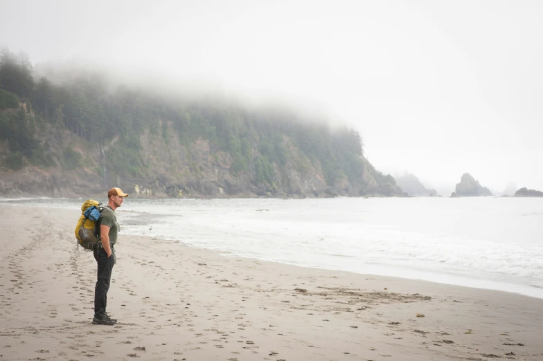 a woman is standing on the beach with her backpack