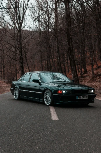 the black bmw is on the road, and it has its lights on