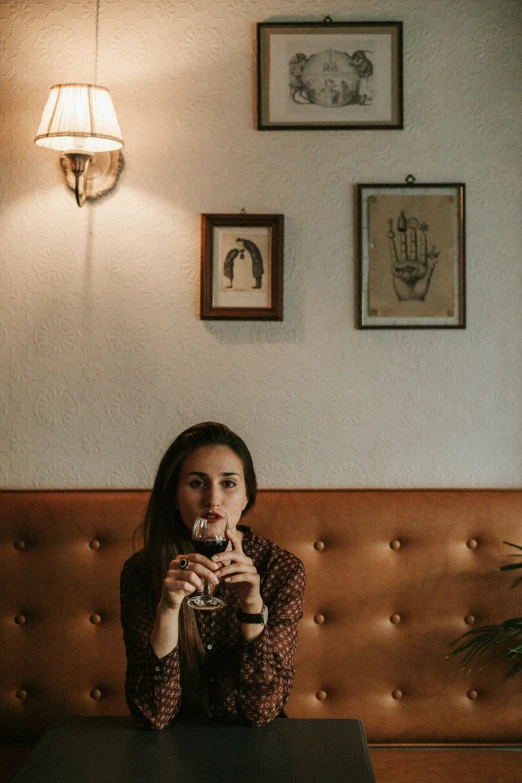 a woman sitting at a table holding a glass in front of her face