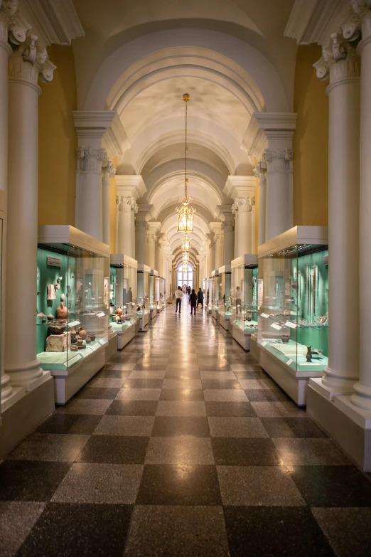 a large museum with green displays on tables and people walking in it