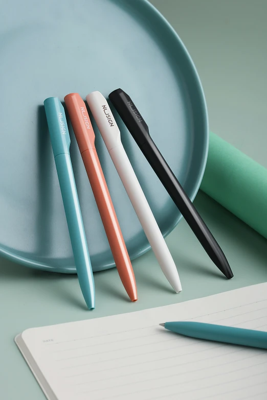 three pens are on a plate and pen is laying on a notepad