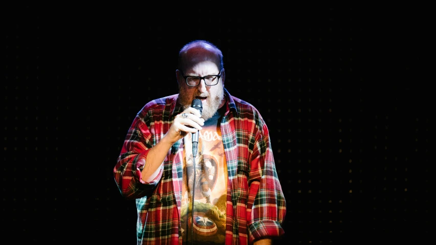 a bearded man wearing a multi - colored plaid shirt singing