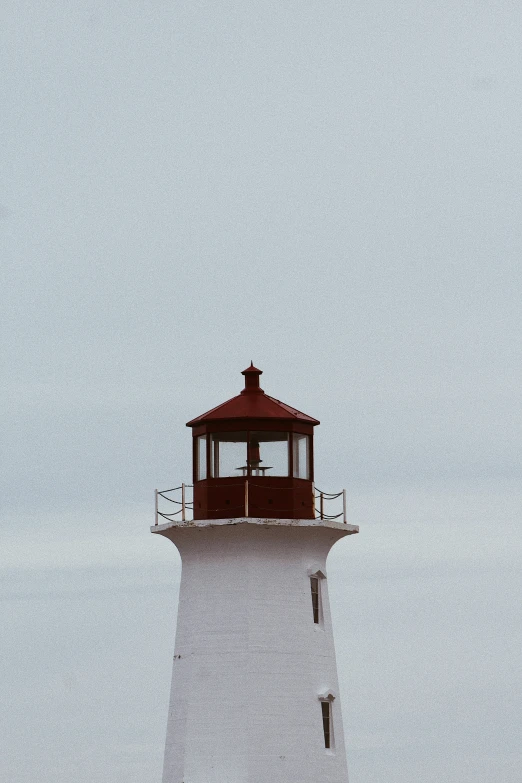 a white lighthouse with red top and lights in the fog