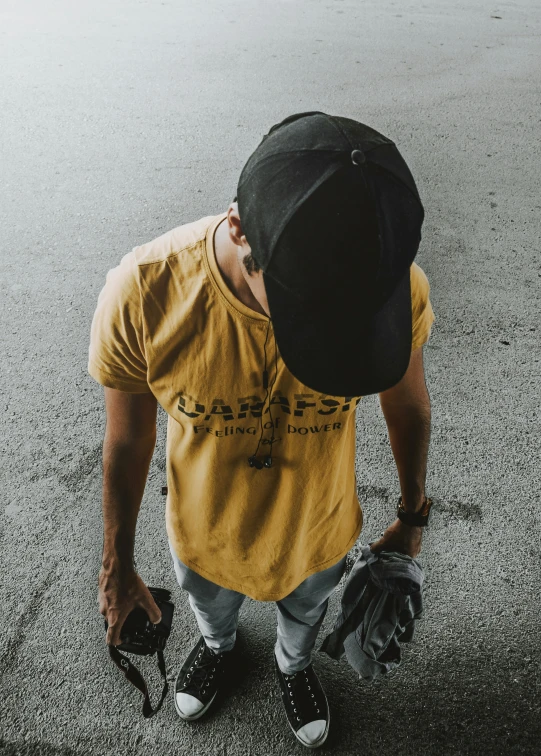 man wearing yellow t shirt and black hat standing on sidewalk