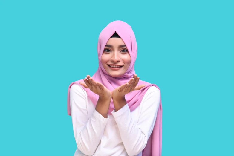 a smiling woman wearing a hijab and dress, making the hand gesture