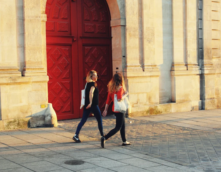 two young women are walking by an old building