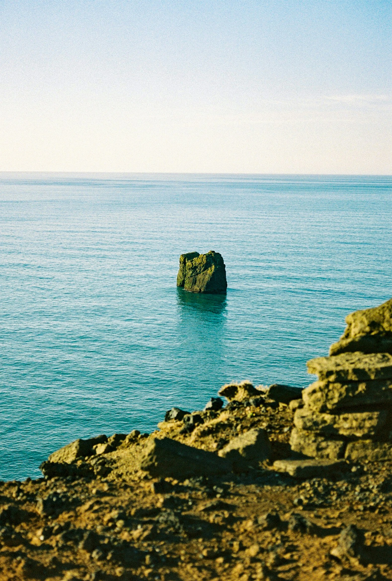 an ocean with a large rock formation and people standing near the shore