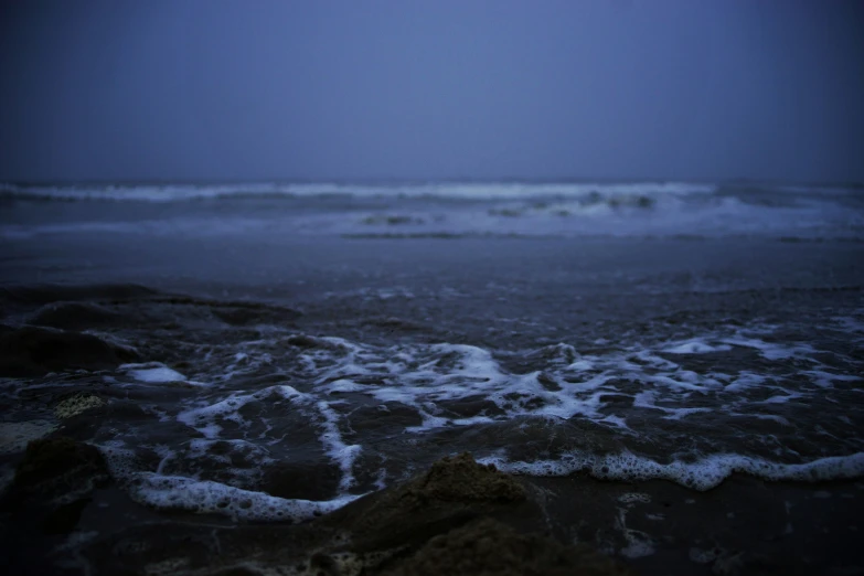 a small wave breaking on the shore at night