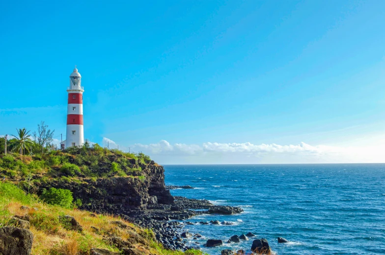 a white lighthouse is at the end of a rocky hill