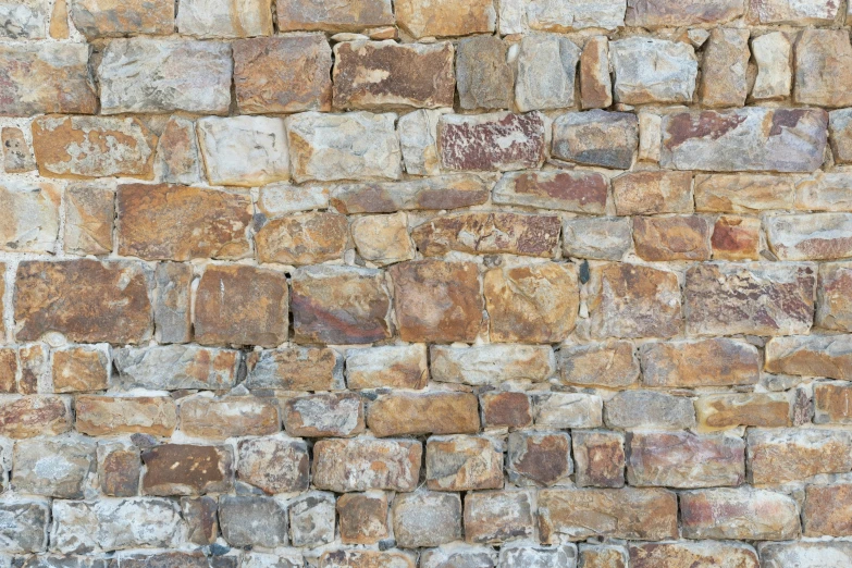 an orange and black cat sitting in front of an old stone wall