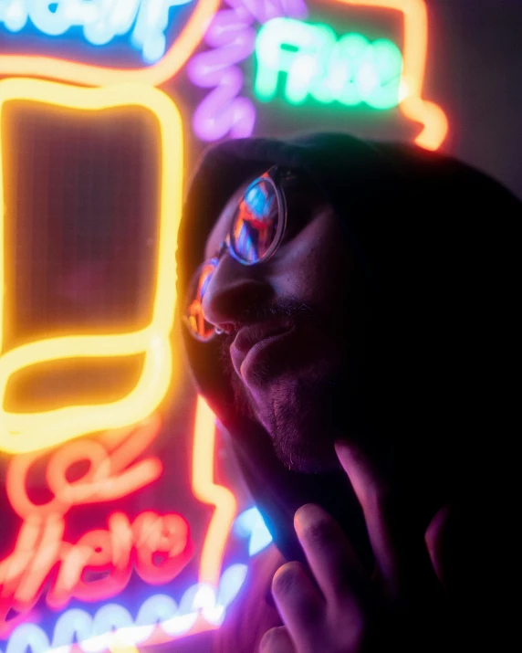 a man with glasses standing in front of neon signs