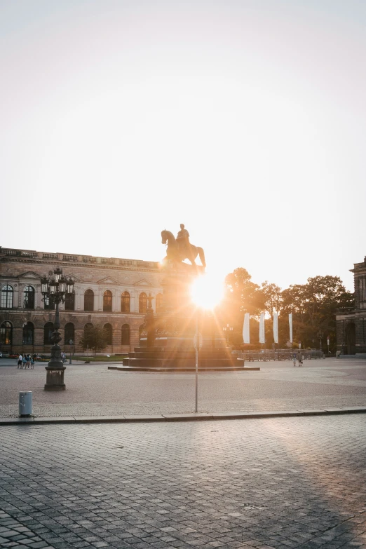 the sun is setting on a statue outside of a large building