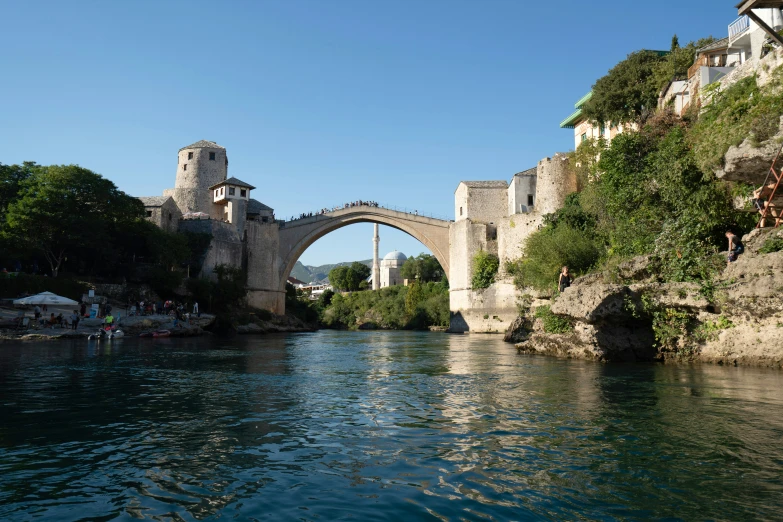 a bridge and buildings along the riverbank near some trees