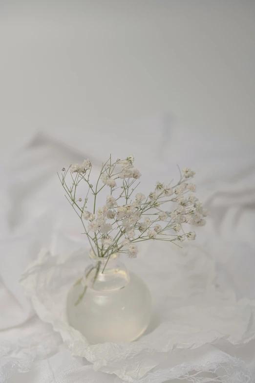 a white cloth with a white vase holding a few flowers