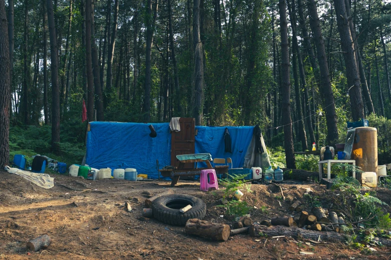 a tent and fire pit in the woods with blue tarp