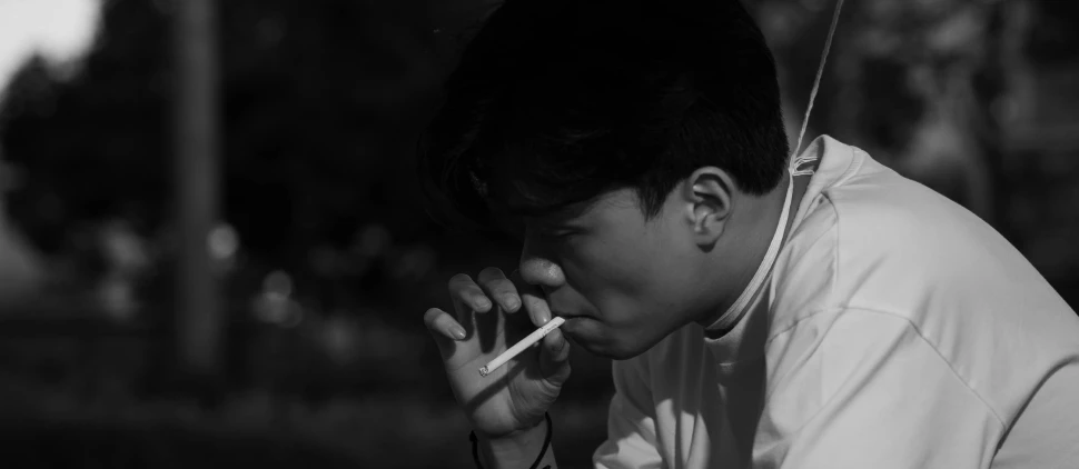 a man smoking while leaning over a pole