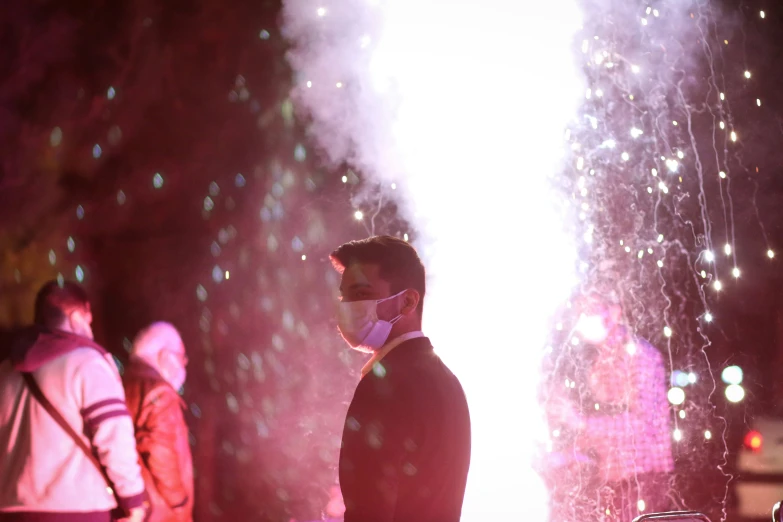 a man is standing watching some fireworks with other people looking on