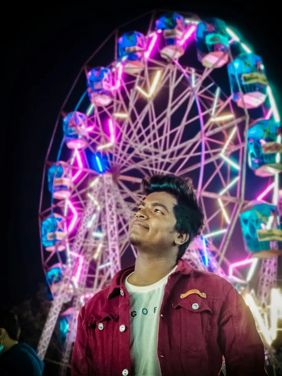 a man with a red shirt standing in front of a ferris wheel