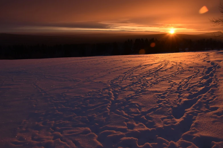 the sun is setting behind a hill covered in snow