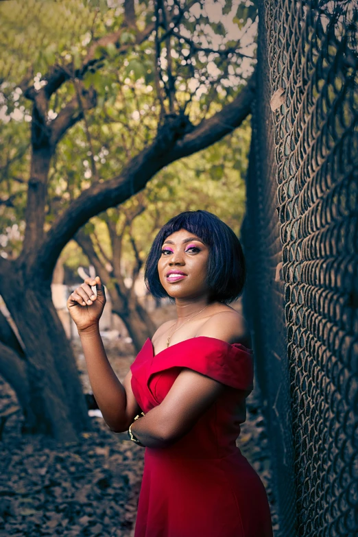 a lady in a red dress smoking a cigarette by a fence