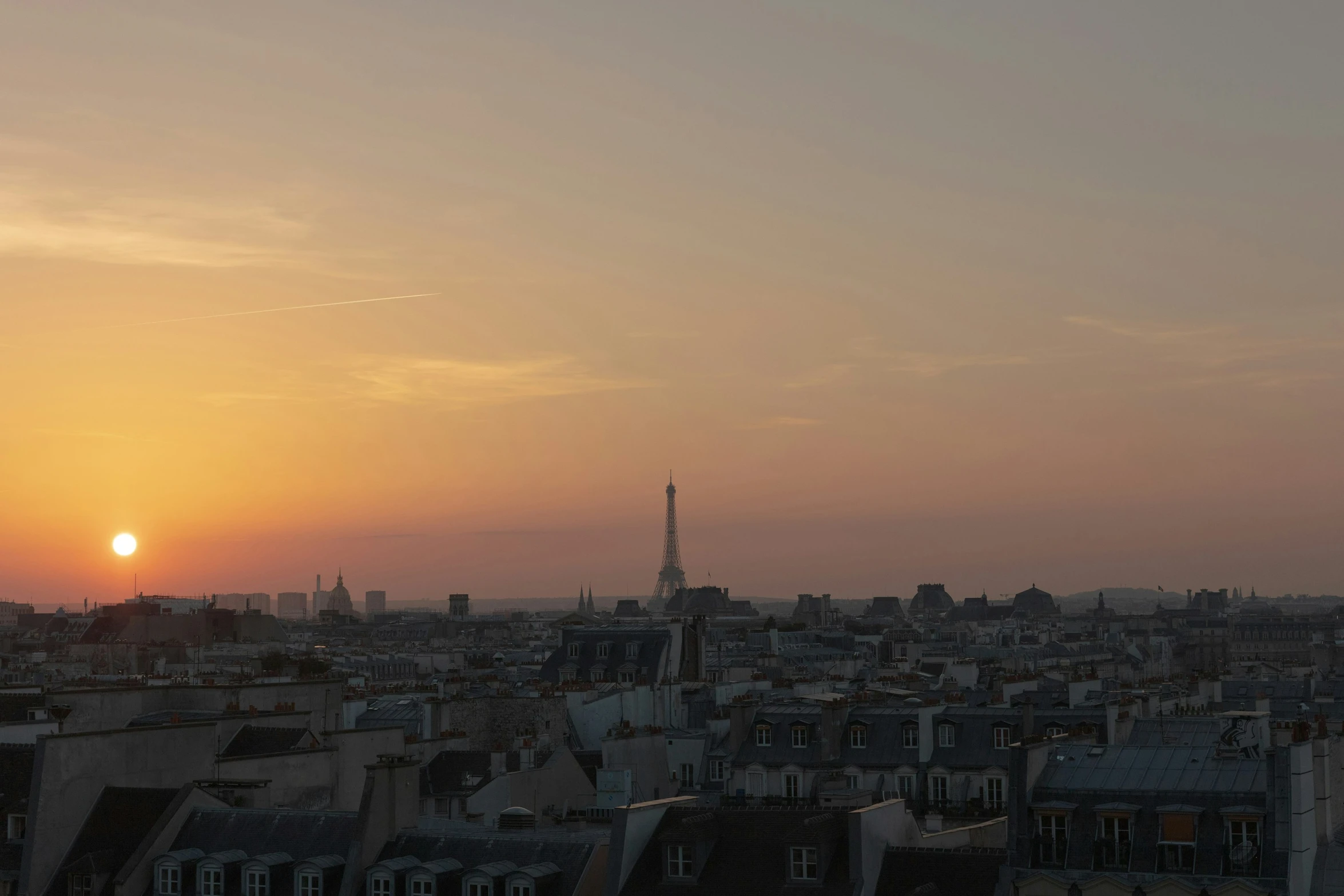 a skyline shows the setting sun with buildings in silhouette