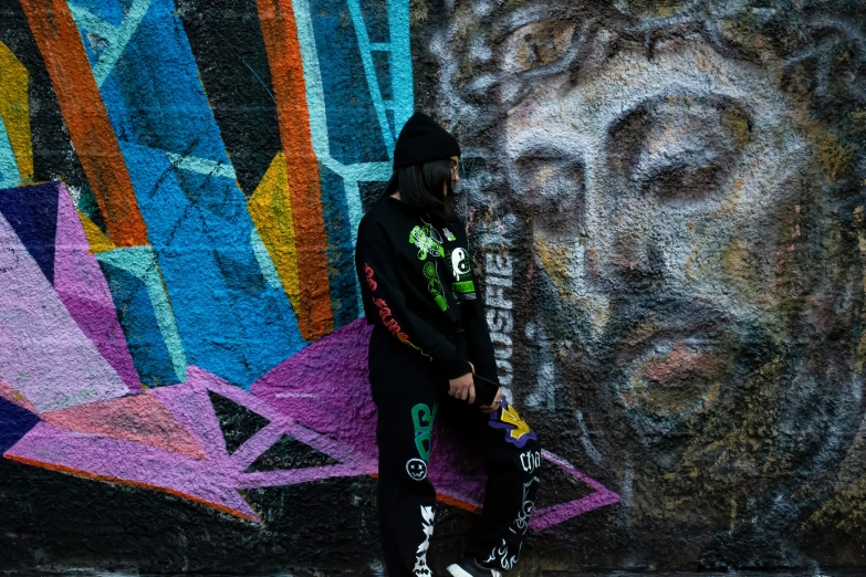 a man in black and green with hoodie leaning on a wall