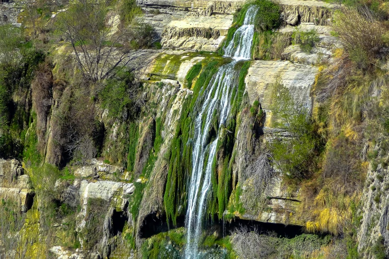 a waterfall flowing into a valley covered in grass and bushes