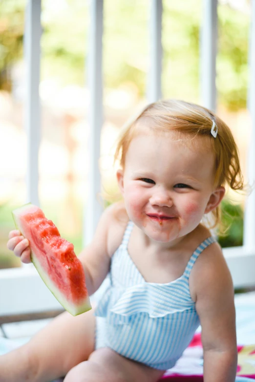 a child is sitting and holding a piece of watermelon