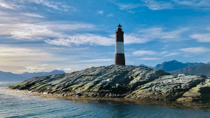 a lighthouse sits atop a rocky outcrop on a calm day