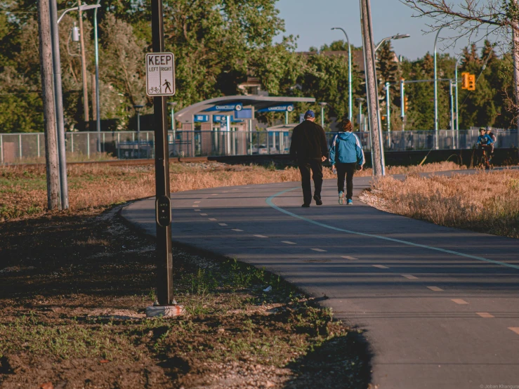 two people walk down a sidewalk next to railroad tracks