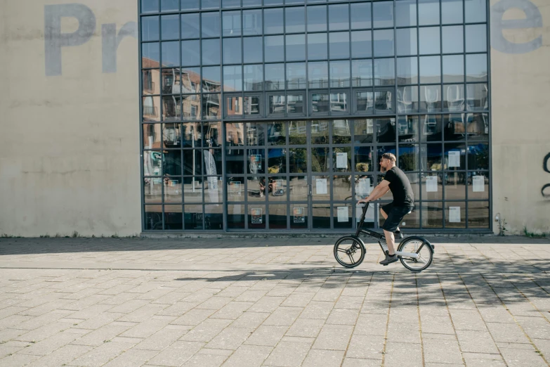 the man is biking on the cobblestone road by the large building