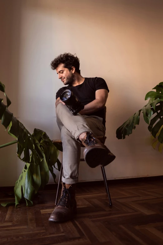 a man holding a camera sits on a chair next to plants