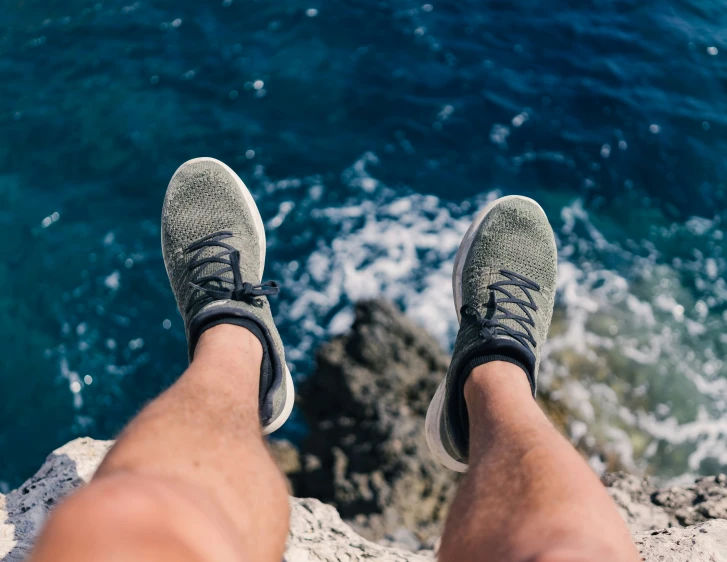 the top view of two feet in sneakers by the ocean