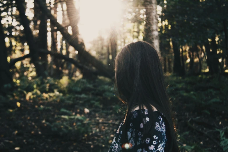 a woman with long hair stands alone in the woods