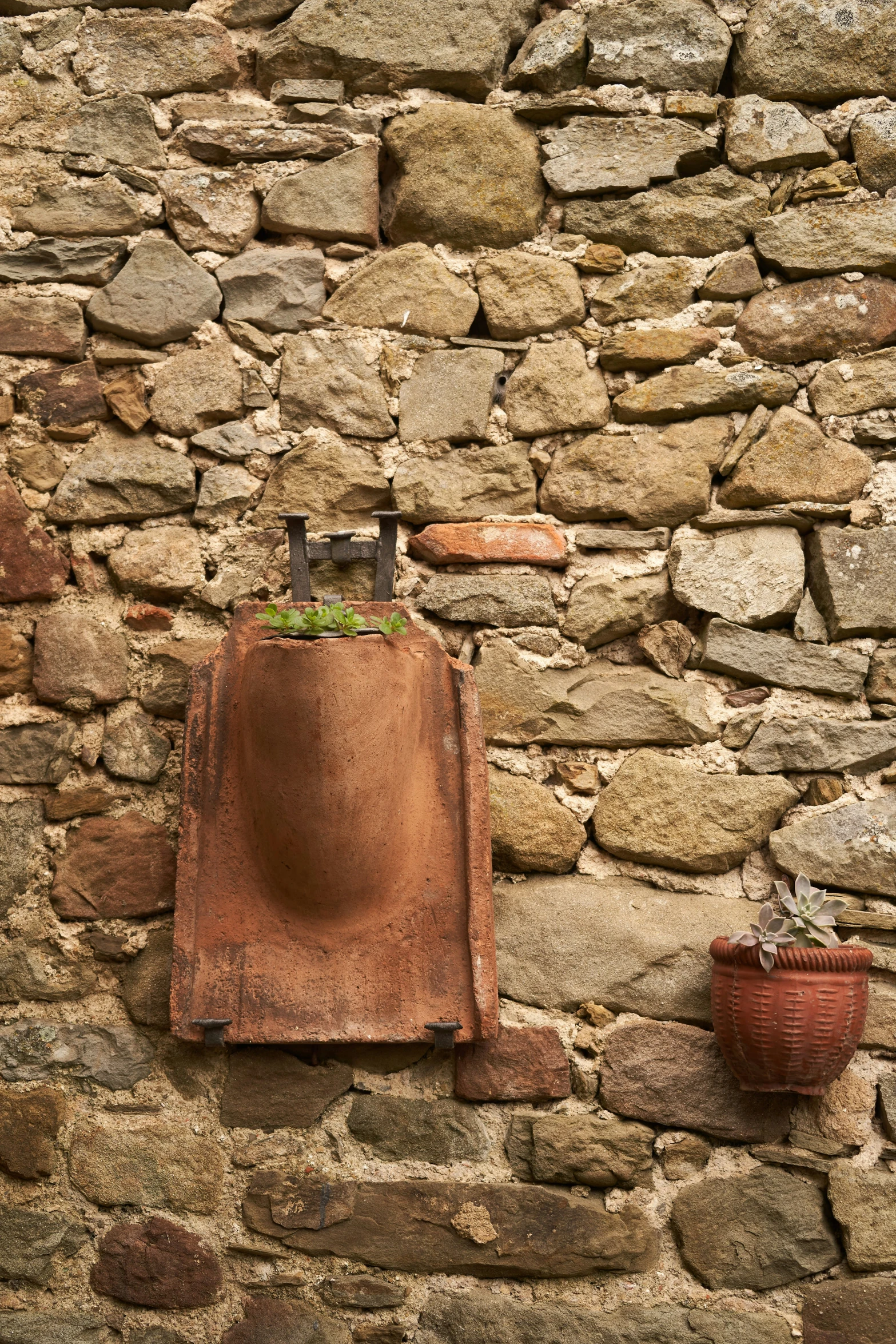 a brick wall has two potted plants and a water faucet