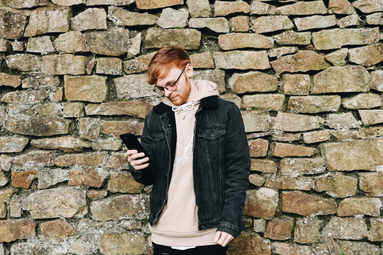 a man using a cell phone next to a stone wall