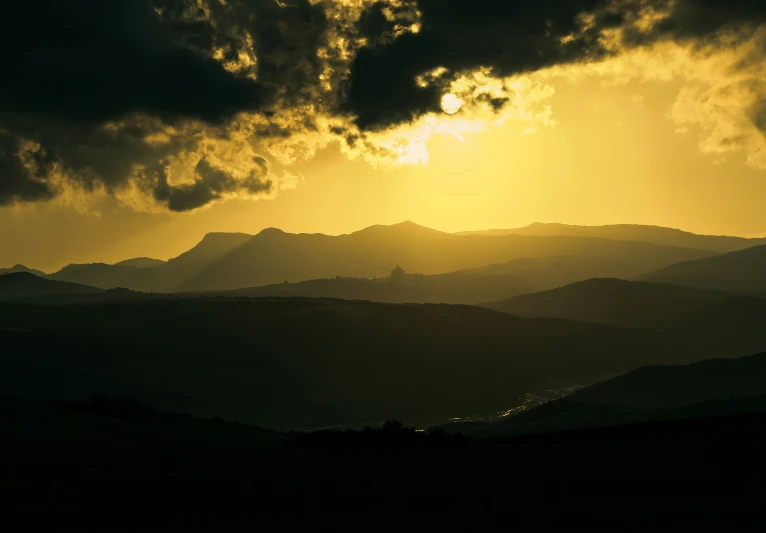 sun shining through a cloudy sky above some mountains