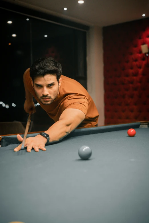a man leans forward as he reaches over the cues to play pool