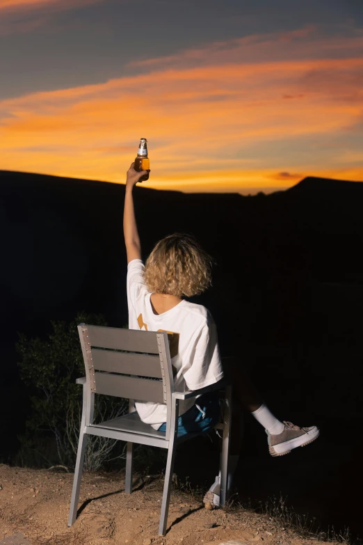 a boy sits on a bench and holds up his beer bottle