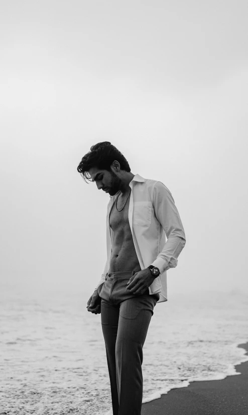 a black and white po of a man standing on the beach looking down