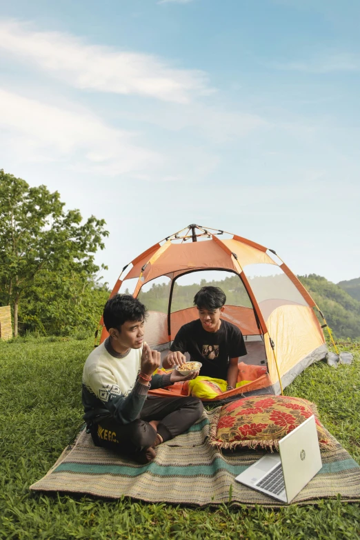 two men sit in a tent and eat outdoors