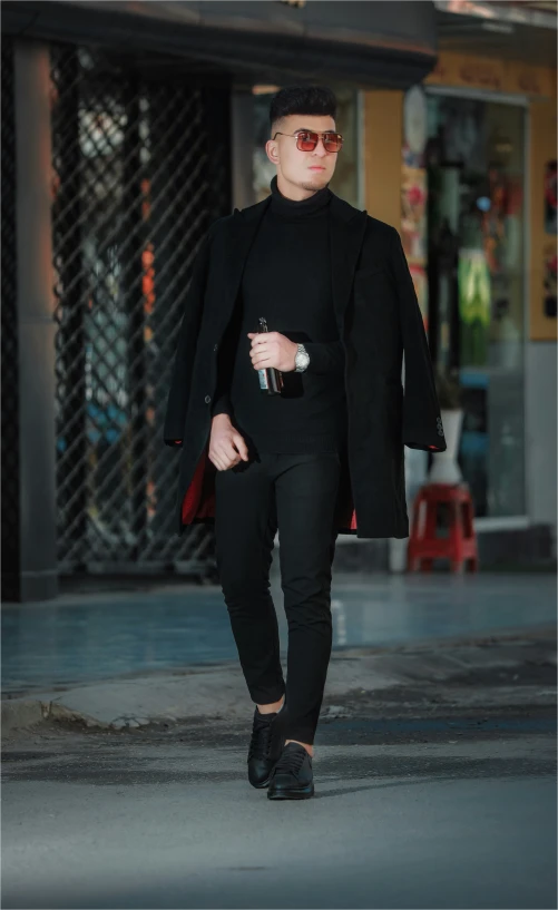 a man in black coat and pants walking down street