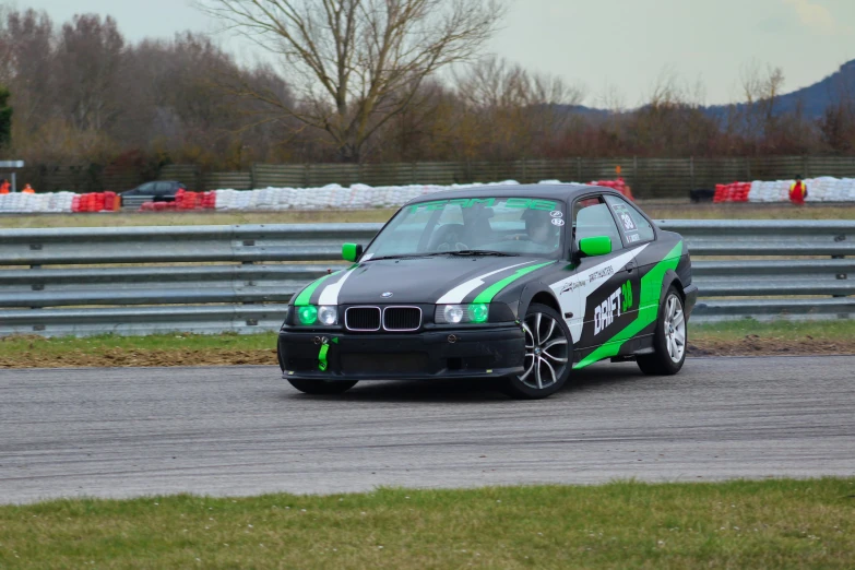 a bmw e36 with green stripe racing on the track