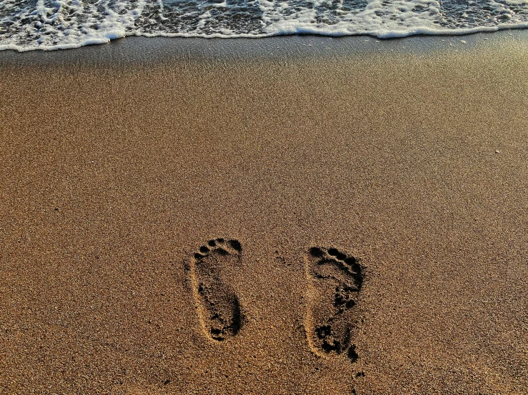 a person's footprints in the sand next to the ocean