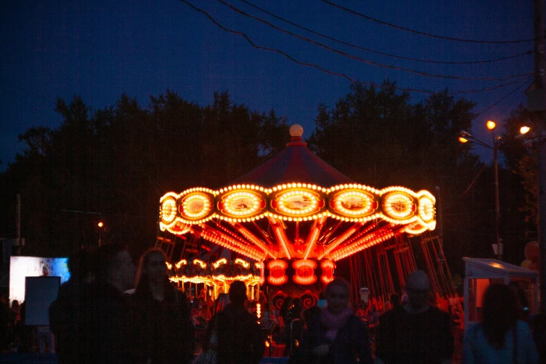 people stand around a lit up carnival ride
