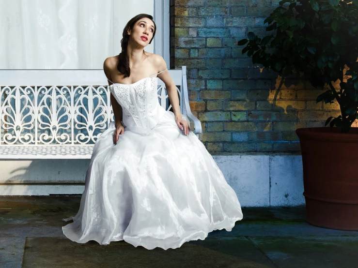 a woman wearing a white dress posing on a white bench