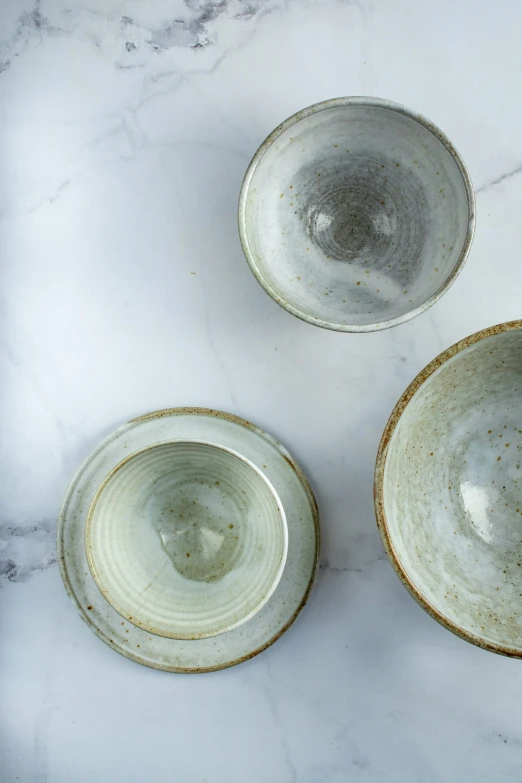 three white bowls on a marble surface with a black dot