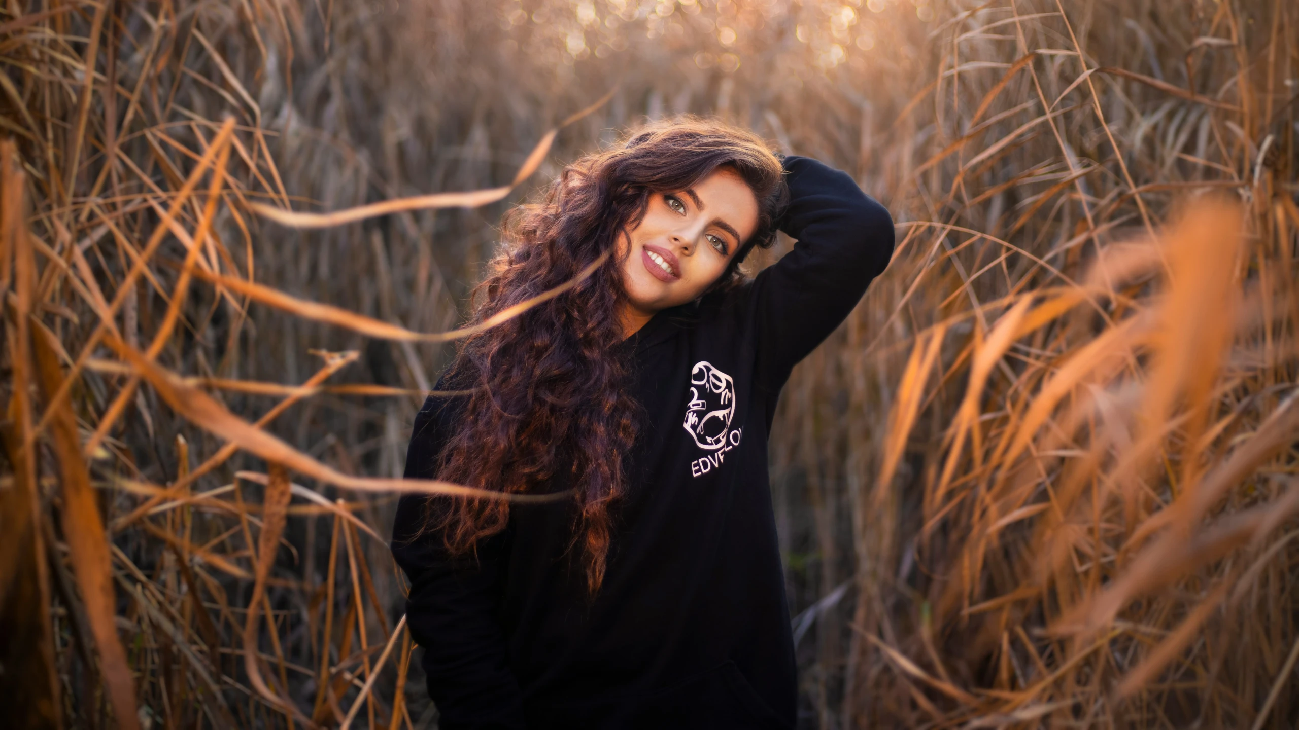 a smiling woman wearing a black shirt in front of tall grass