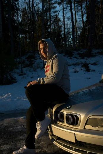 a young man sits on the hood of his bmw